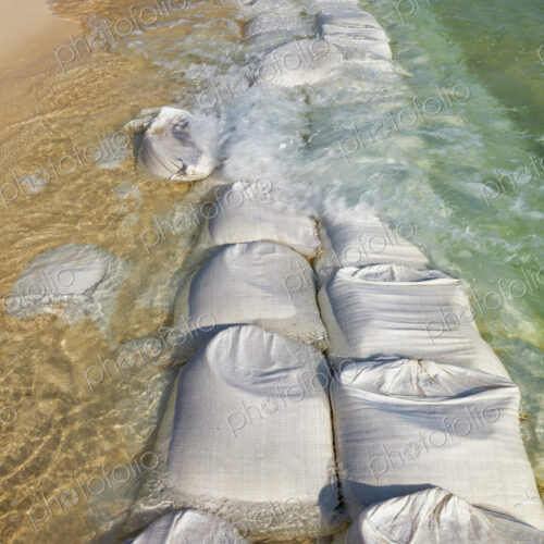 Sandbags in rows at the water's edge to prevent erosion of the beach