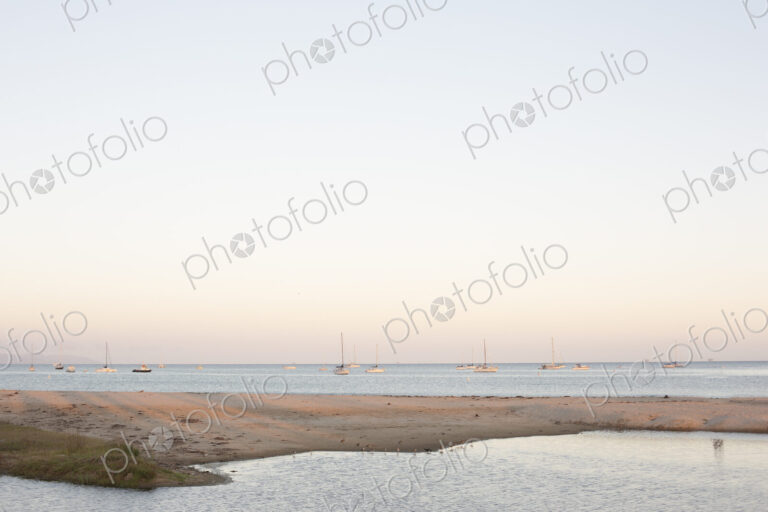 Sandy beach and ocean, sailing boats in the distance.