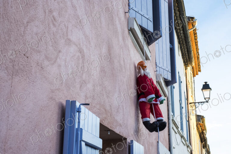 Santa Clause figure hanging on rope from a window of house with pink facade.