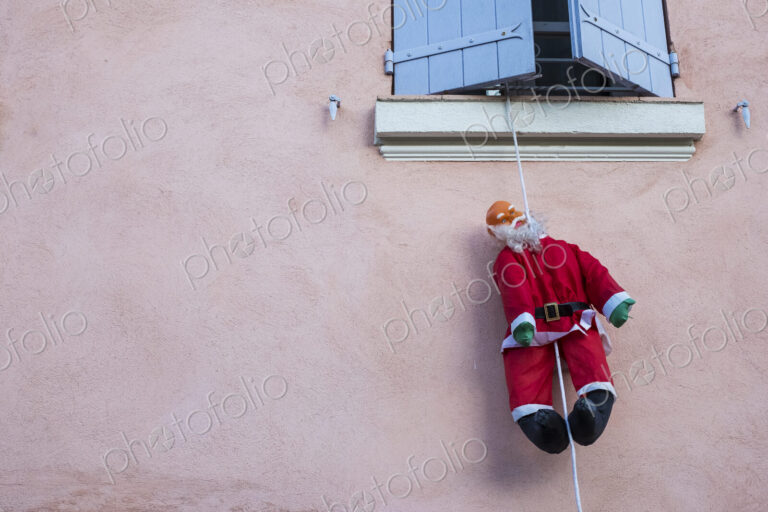 Santa Clause figure hanging on rope from a window of house with pink facade.