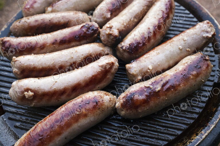 Sausages arranged on top of a barbeque grill, cooking outdoors.