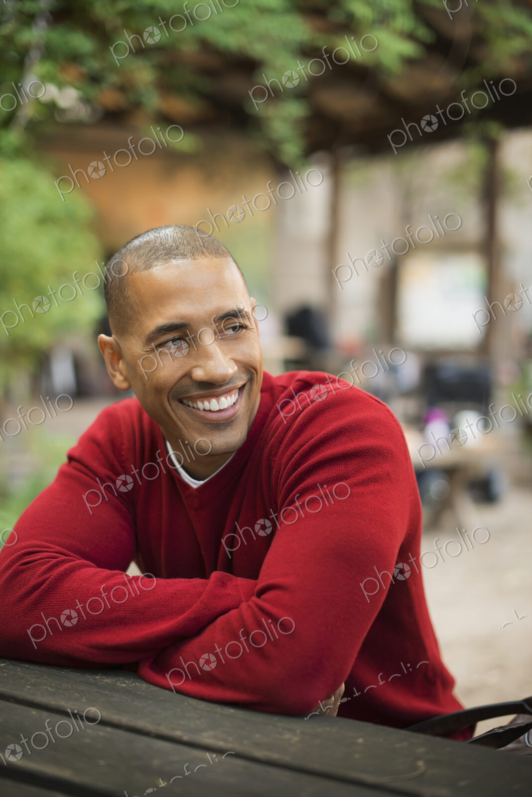 Scenes from urban life in New York City. A man in a red jumper seated at a bench, smiling.