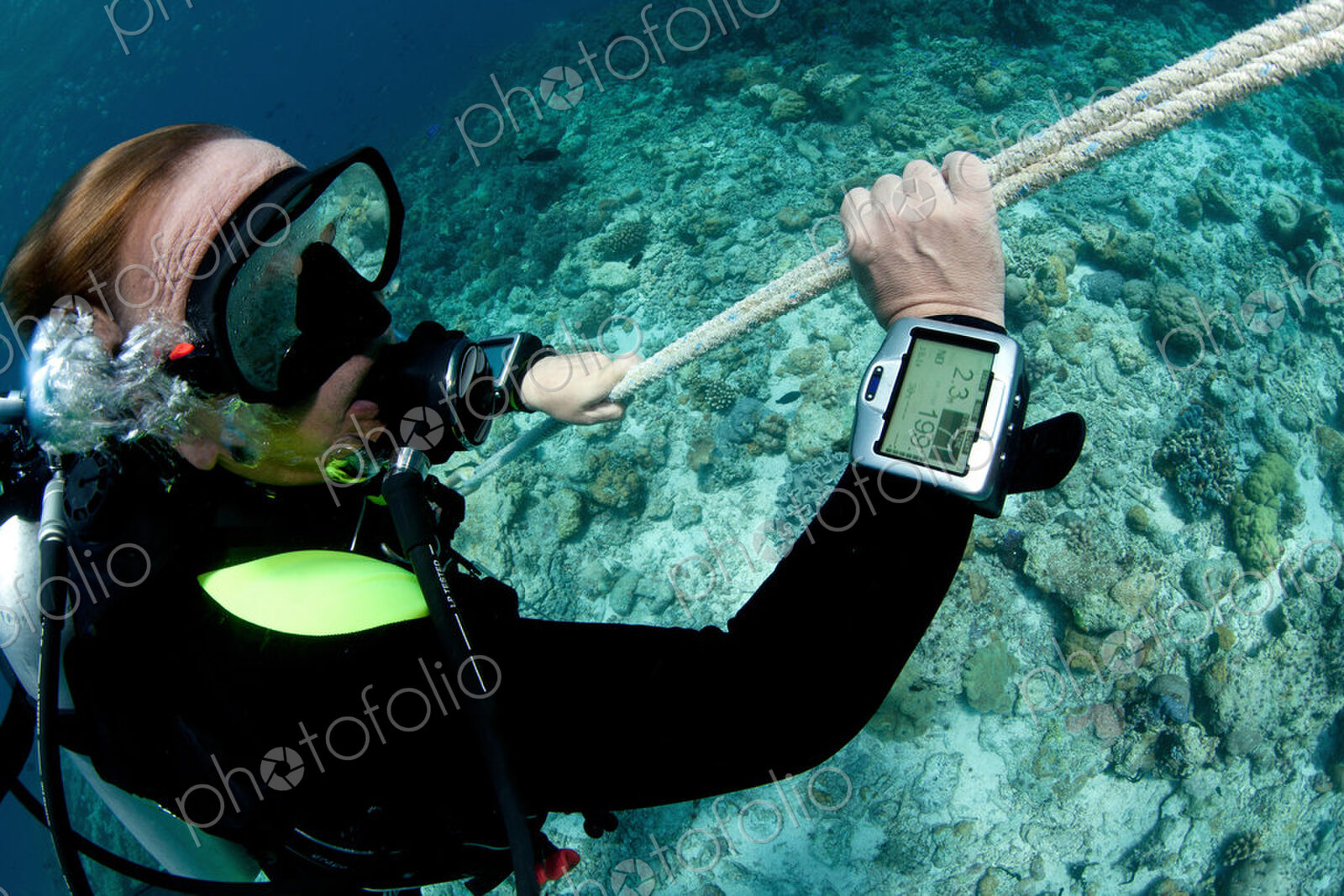 Scuba diver monitors his dive computer screen with information on time and depth while…