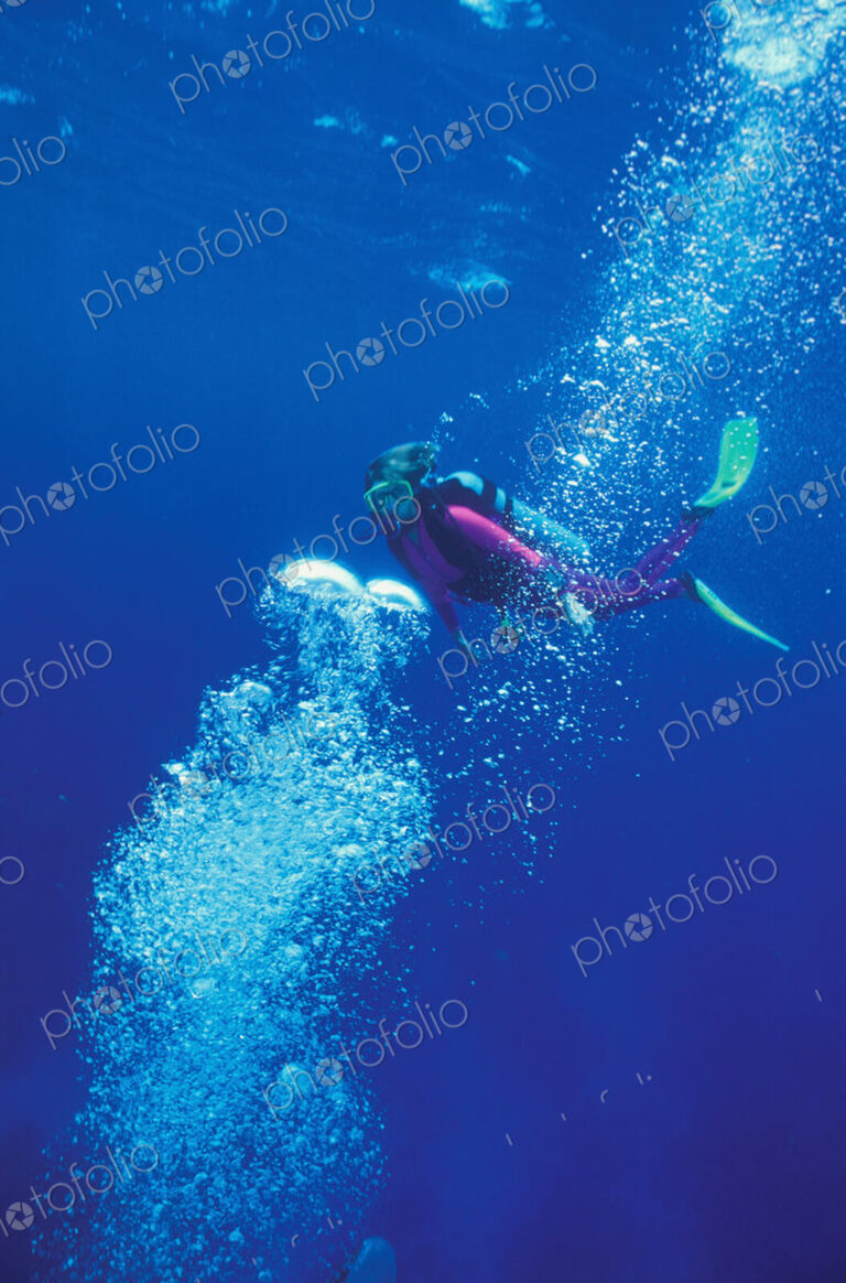Scuba diver swims through a stream of bubbles.