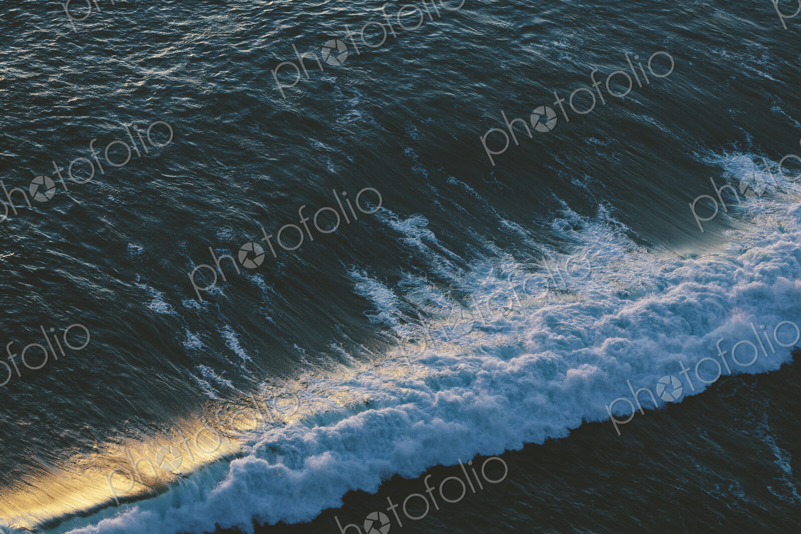 Seascape abstract at dusk, surf breaking on the shore, overhead view and sunlight on…