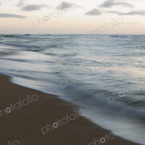 Seascape and crashing waves on beach at dusk.