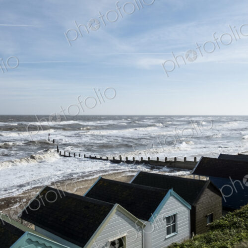 Seascape over a row of wooden beach huts, with waves rolling onto beach near groyne. Seascape over a row of wooden beach huts, with waves rolling onto beach near groyne.