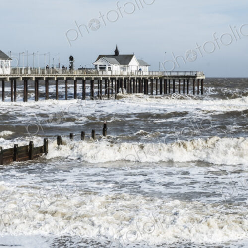 Seascape with waves rolling onto beach near groyne and white wooden buildings on a pier. Seascape with waves rolling onto beach near groyne and white wooden buildings on a pier.