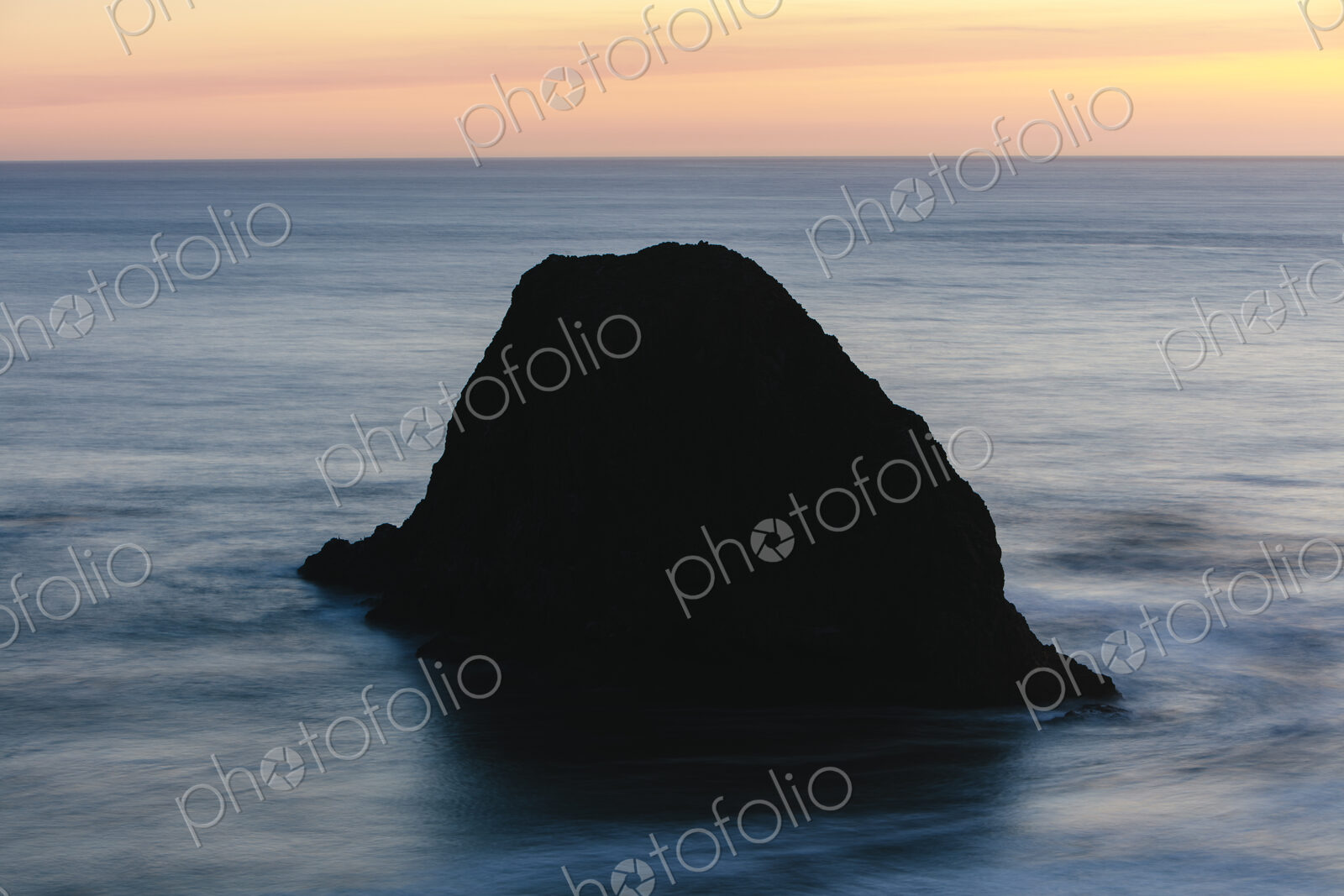 Seastack in vast ocean at dusk