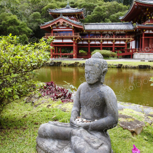 Seated sculpture of a religious figure and a temple building in trees by a lake
