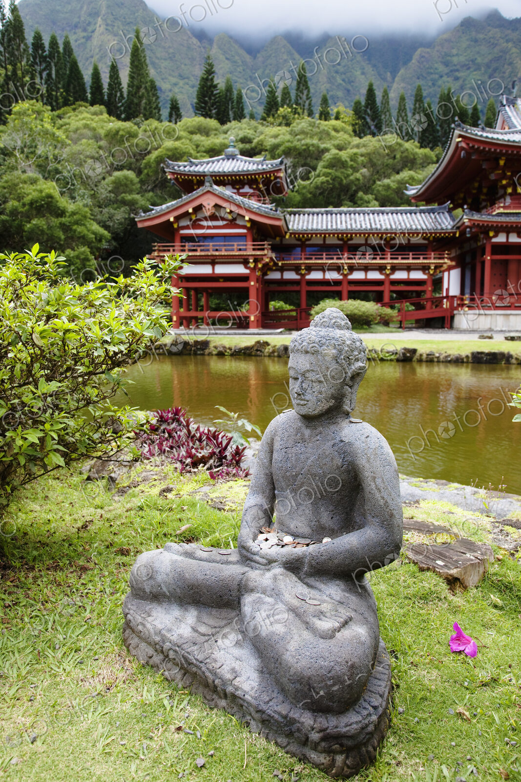 Seated sculpture of a religious figure and a temple building in trees by a lake