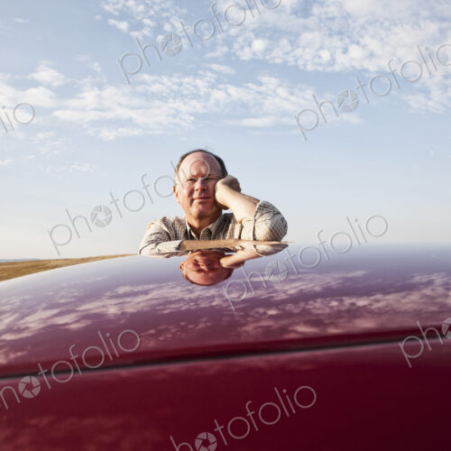 Senior Caucasian man leaning on roof of his car