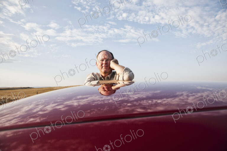 Senior Caucasian man leaning on roof of his car