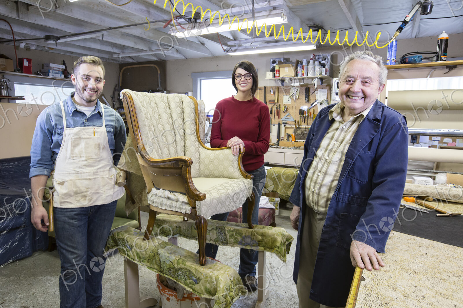 Senior Caucasian man upholsterer and his understudy team of young people working on an…