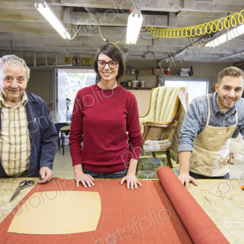 Senior Caucasian man upholsterer and his understudy team of young people working on an…