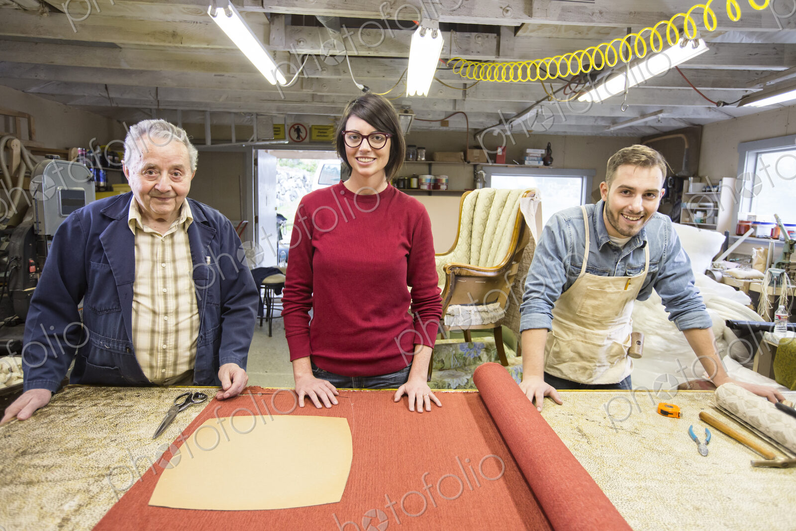 Senior Caucasian man upholsterer and his understudy team of young people working on an…