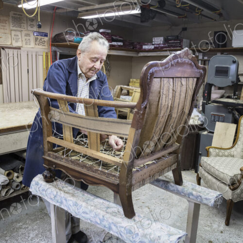 Senior Caucasian man upholsterer working on an antigue chair in his garage shop. Senior Caucasian man upholsterer working on an antigue chair in his garage shop.