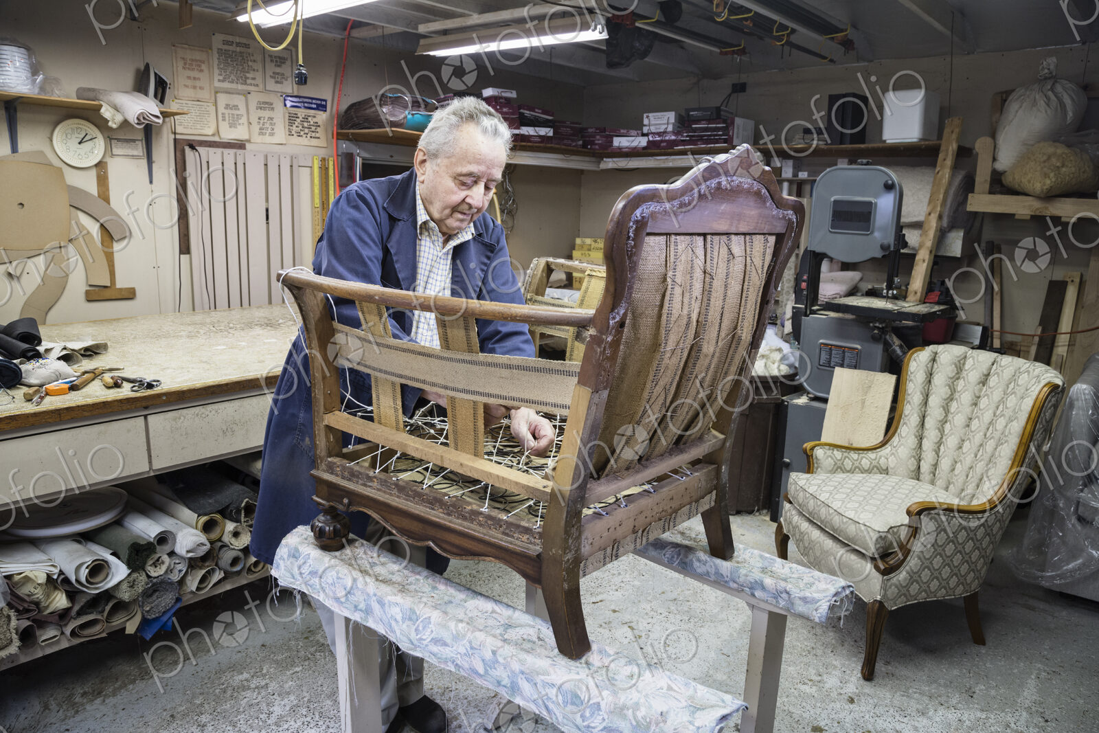 Senior Caucasian man upholsterer working on an antigue chair in his garage shop.