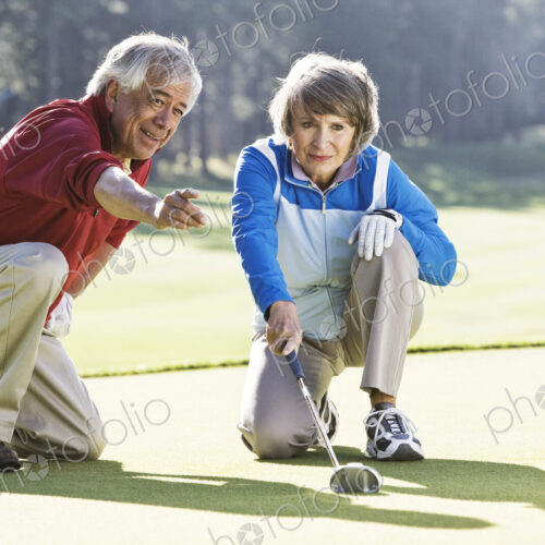 Senior couple discussing the direction of the putt on the green of a golf course.