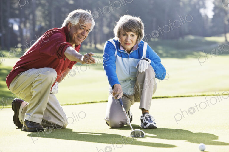 Senior couple discussing the direction of the putt on the green of a golf course.