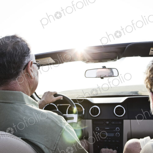 Senior couple in a convertible sports car driving on a highway at sunset