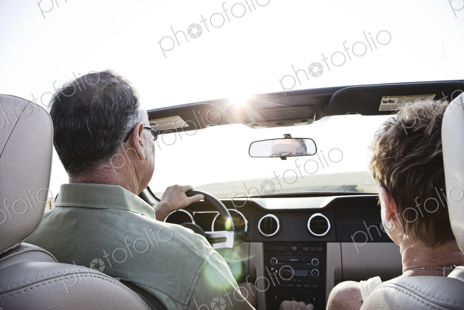 Senior couple in a convertible sports car driving on a highway at sunset