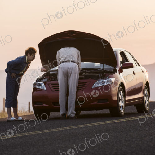 Senior couple with car engine problems while on a road trip.