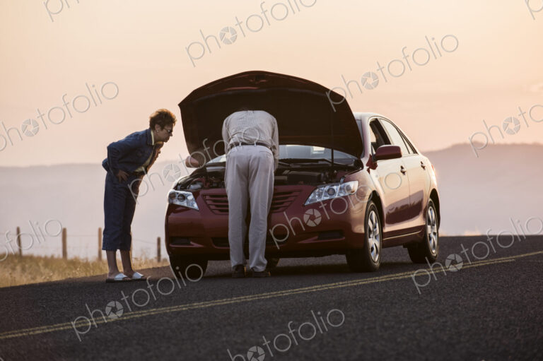 Senior couple with car engine problems while on a road trip.
