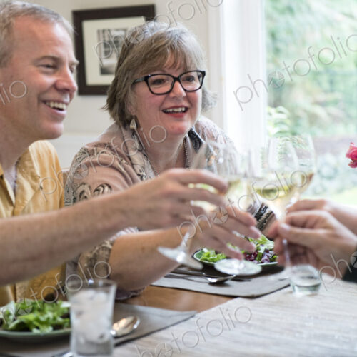Senior couples toasting a home dinner party with glasses of white wine.