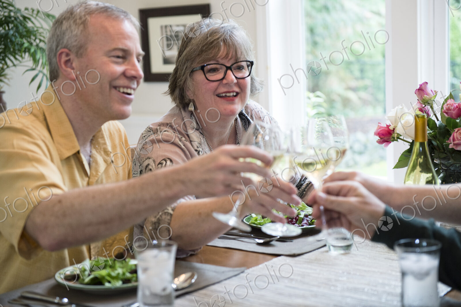Senior couples toasting a home dinner party with glasses of white wine.
