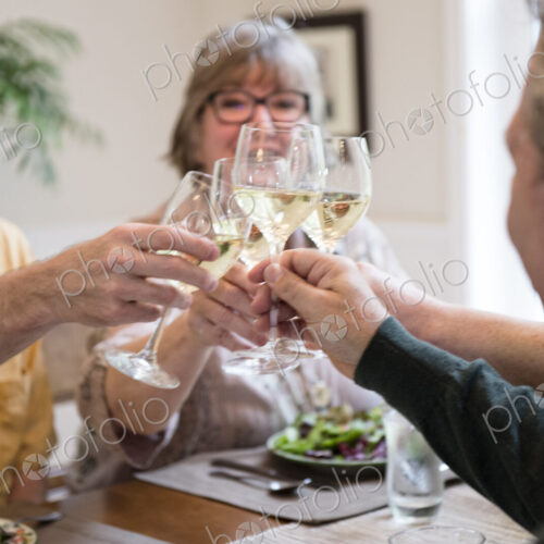 Senior couples toasting a home dinner party with glasses of white wine.
