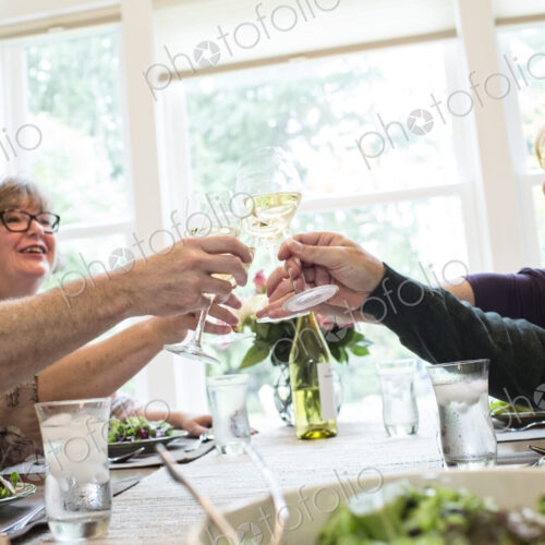 Senior couples toasting a home dinner party with glasses of white wine.