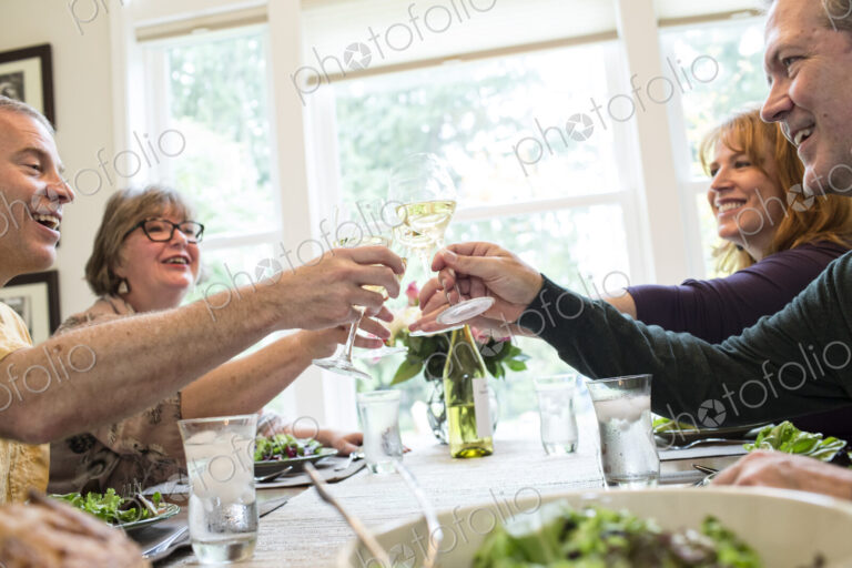 Senior couples toasting a home dinner party with glasses of white wine.