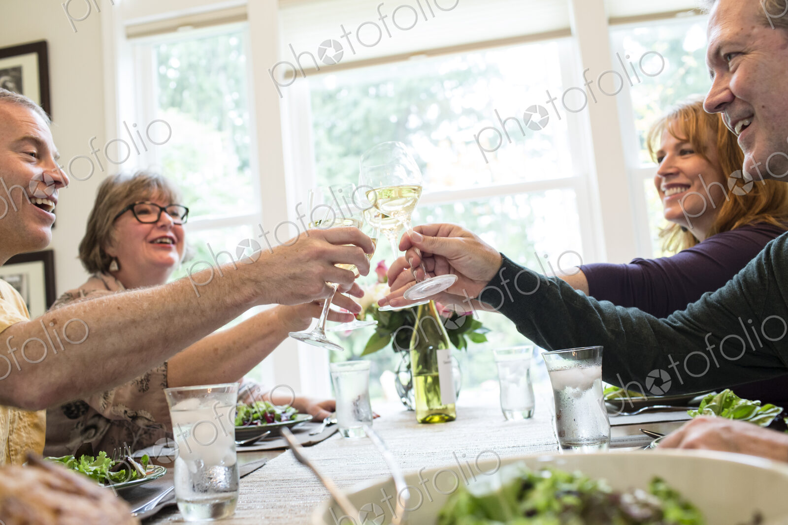 Senior couples toasting a home dinner party with glasses of white wine.