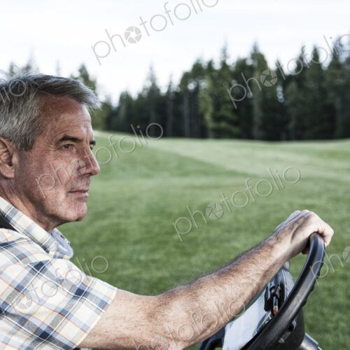 Senior golfer driving a golf cart on the cart path of a golf course. Senior golfer driving a golf cart on the cart path of a golf course.