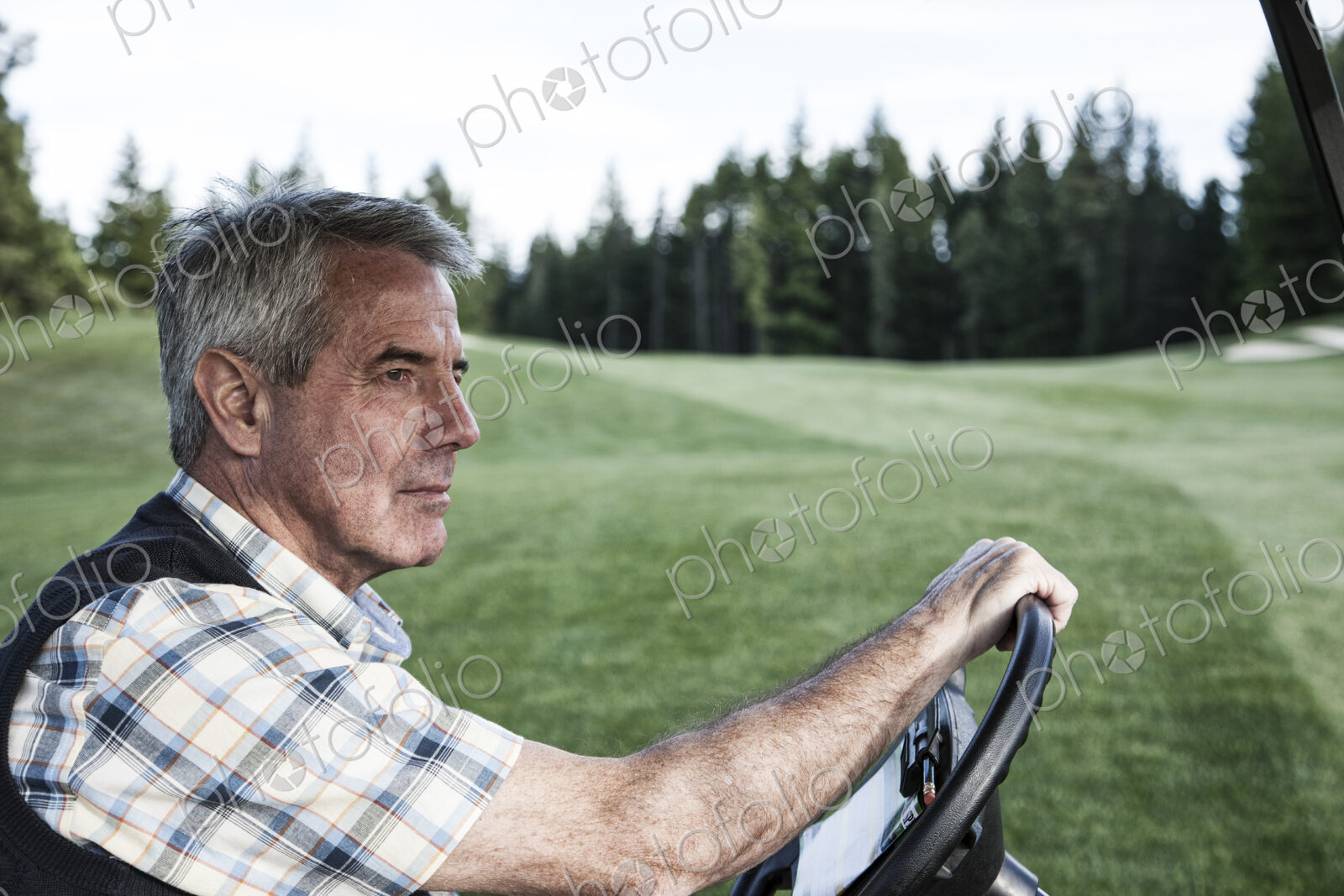 Senior golfer driving a golf cart on the cart path of a golf course.