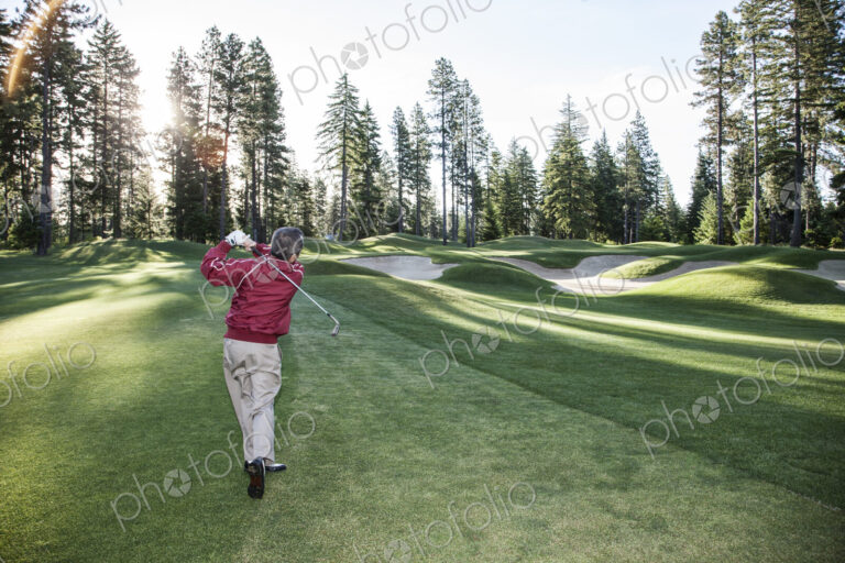 Senior golfer hitting a second shot from the fairway of a golf course.
