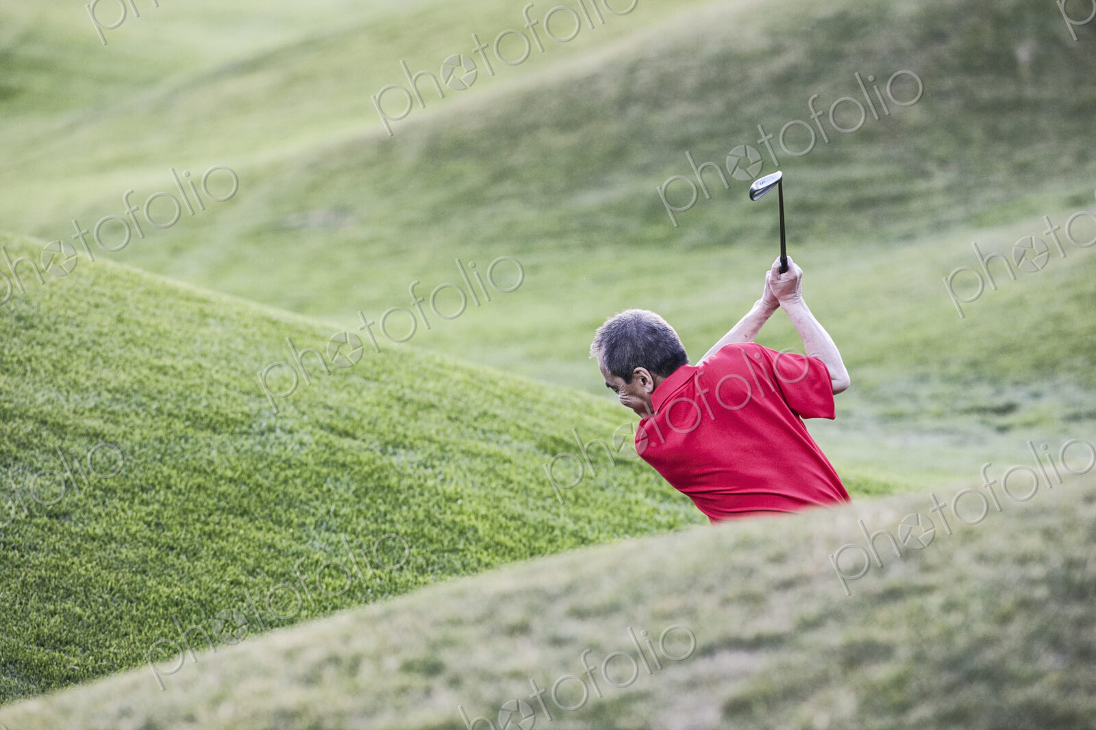 Senior golfer hitting a second shot from the fairway of a golf course.