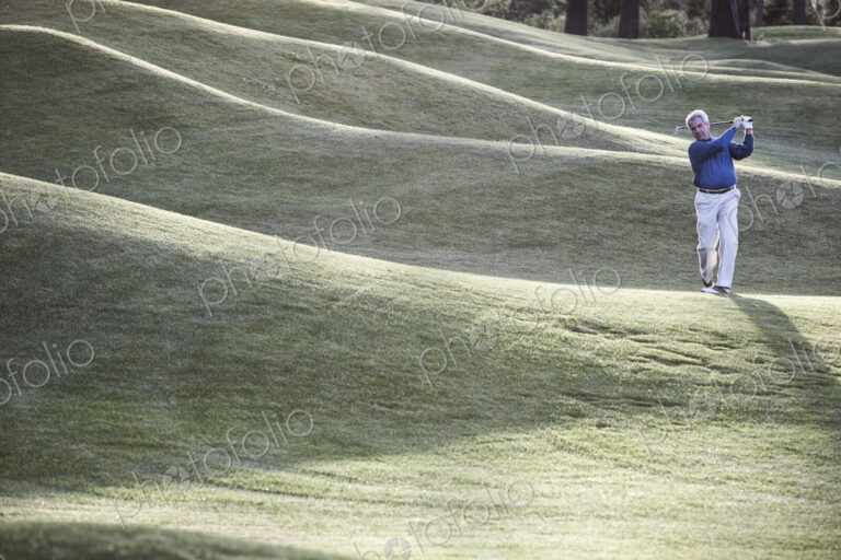 Senior golfer hitting a second shot from the fairway of a golf course.