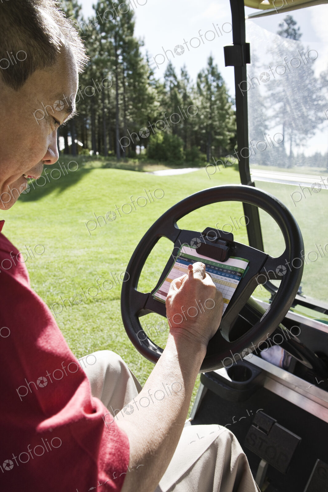 Senior golfer recording his score on a score card in a golf cart.