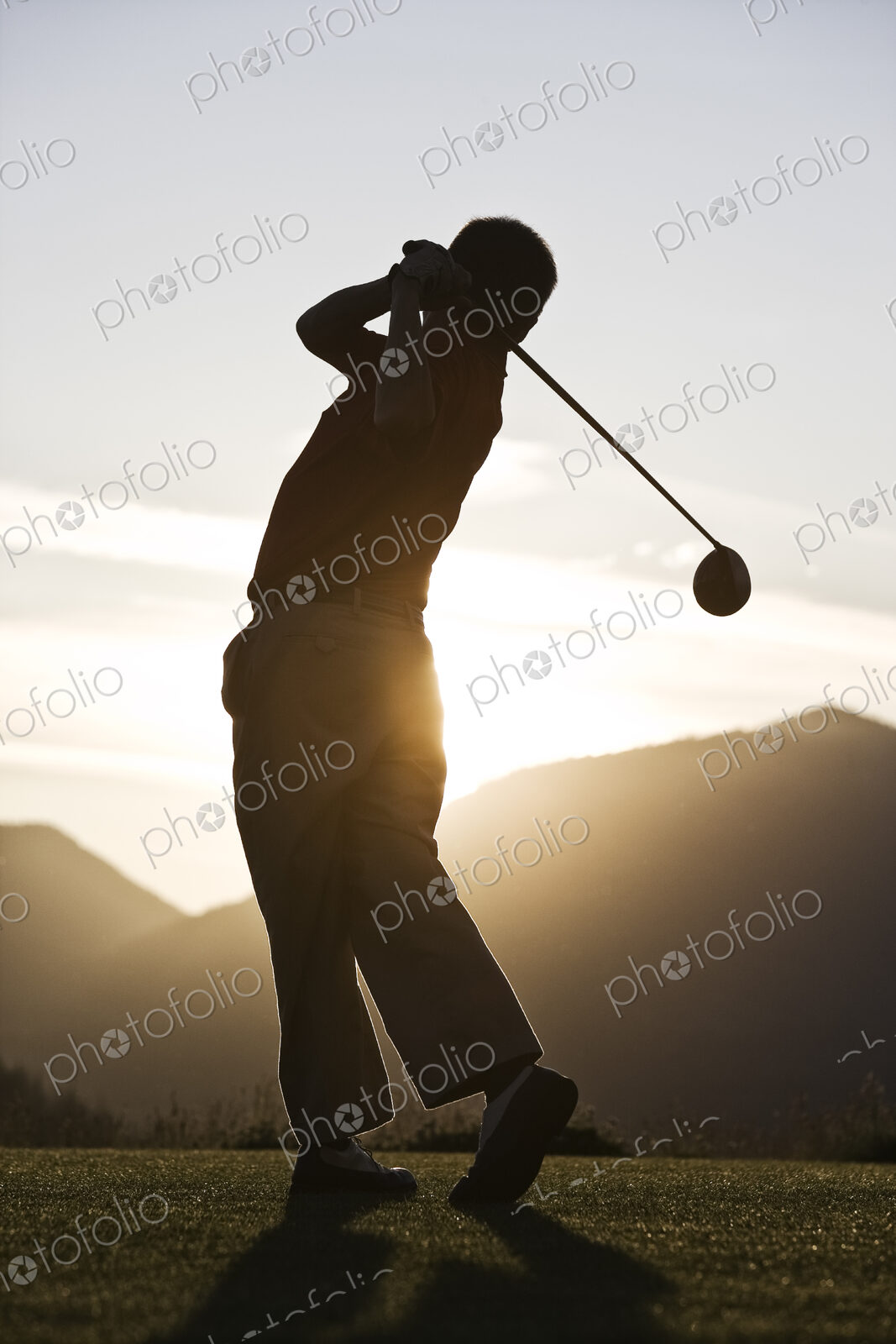 Senior golfer teeing off at sunset.