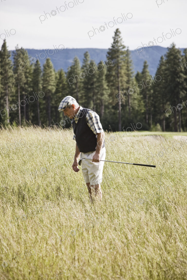 Senior golfer trying to find golf ball that has flown into heavy rough on the golf course.