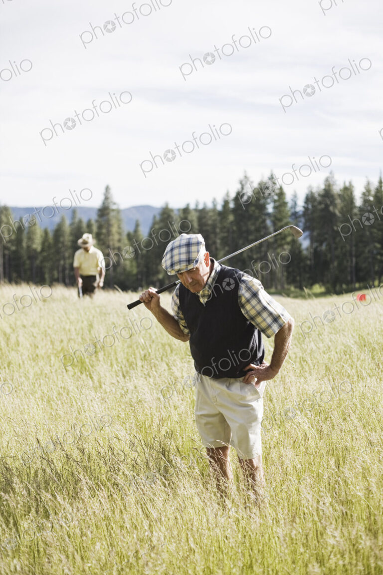 Senior golfer trying to find golf ball that has flown into heavy rough on the golf course.
