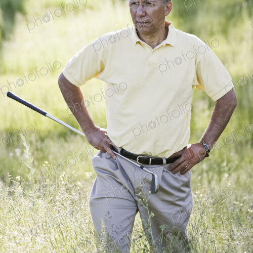 Senior golfer trying to find golf ball that has flown into heavy rough on the golf course.