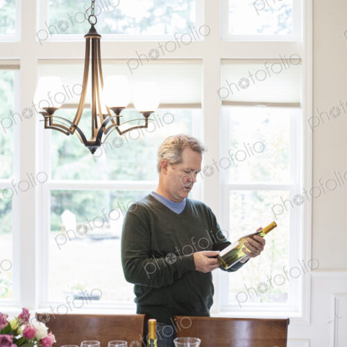 Senior man checking a bottle of wine prior to a home dinner party.