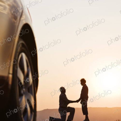Senior man proposing to a woman while watching a sunset on a road trip.