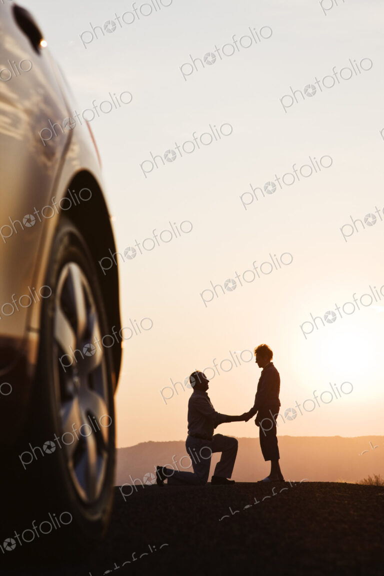 Senior man proposing to a woman while watching a sunset on a road trip.