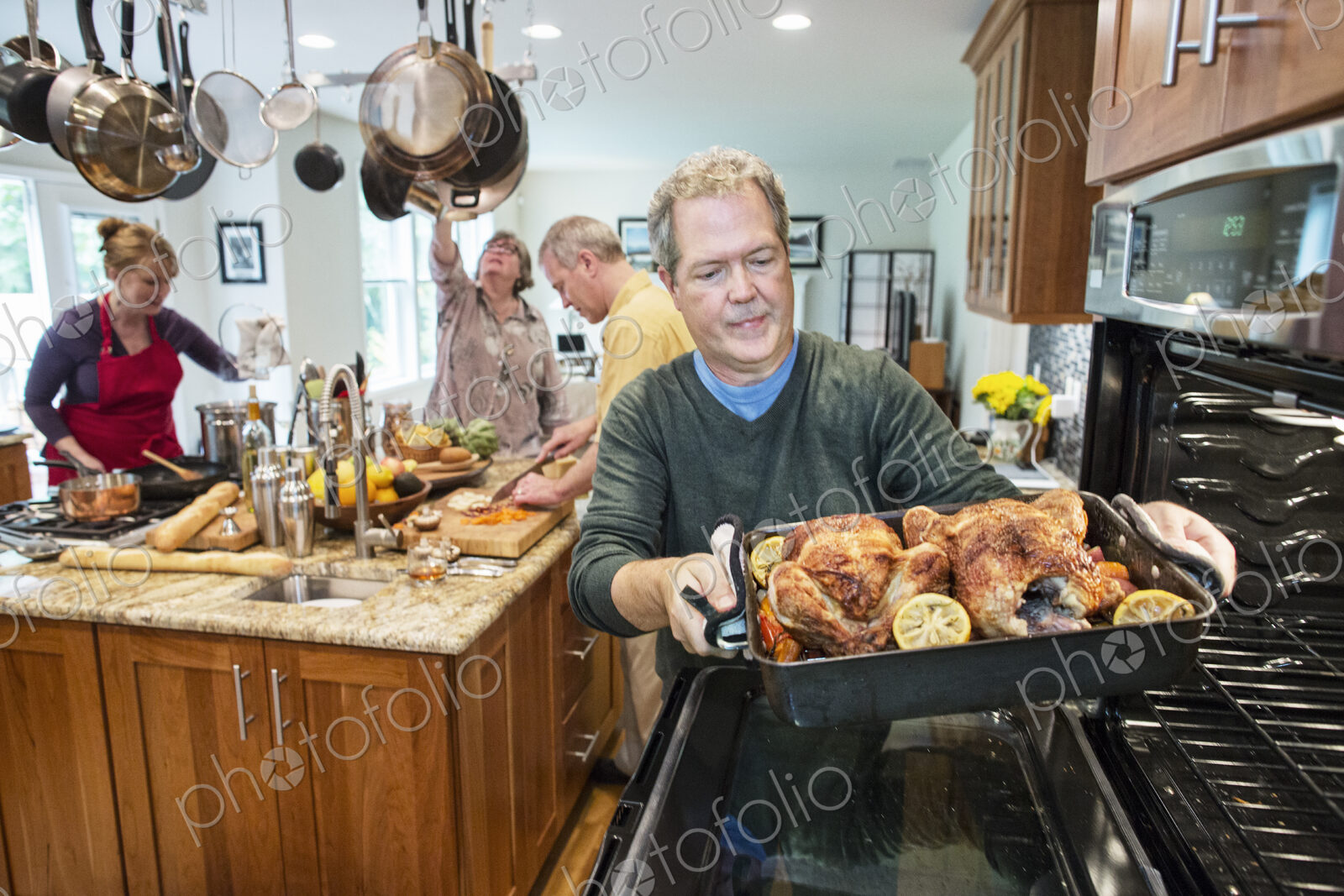 Senior man pull roast chickens out of the oven at a home dinner party.