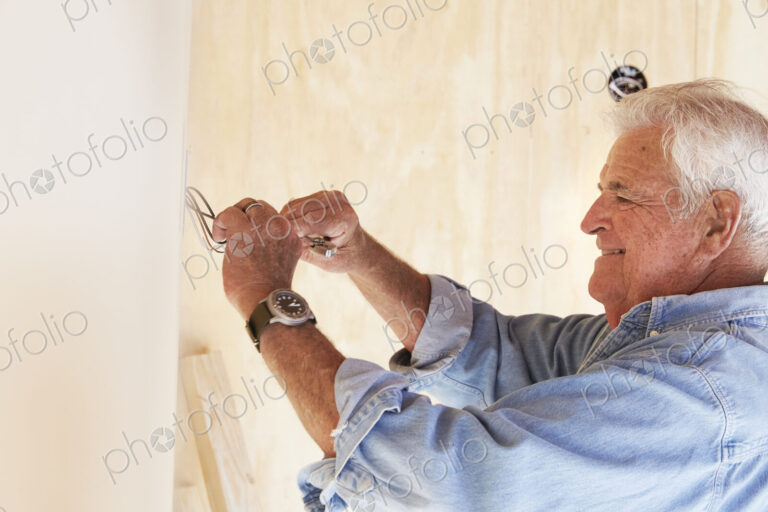 Senior man working on electrical wiring in a house.