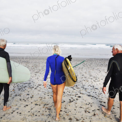 Senior woman and two senior men on a beach, wearing wetsuits and carrying surfboards. Senior woman and two senior men on a beach, wearing wetsuits and carrying surfboards.